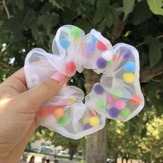 a hand holding up some colorful hair clips in front of a tree with people walking by