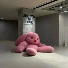 a large pink teddy bear sitting on the ground in an empty room with concrete walls