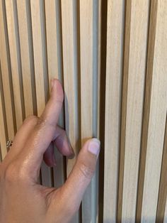 a person's hand is opening the wooden blinds