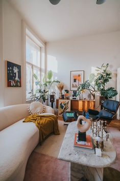 a living room filled with lots of furniture and plants on top of a table in front of a window