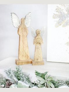 two wooden angel figurines sitting next to each other on a table with pine cones