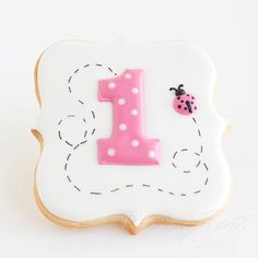 a decorated cookie with the number one in pink and ladybug dots on it