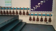 some brown and white guitars are hanging on the wall next to blue stairs in a school hallway