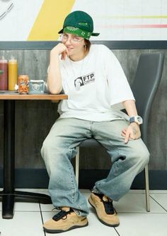 a young man sitting at a table with his hand on his chin and wearing a green hat