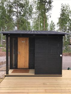 a small black building sitting on top of a wooden deck next to trees and grass