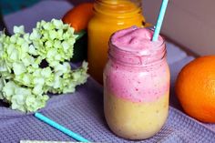 an orange and pink smoothie in a mason jar next to two strawberries on a table