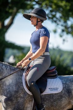 a woman riding on the back of a gray horse wearing a helmet and riding gear