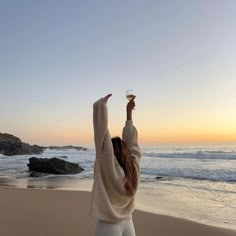 a woman standing on top of a sandy beach holding a wine glass in the air