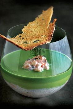 a piece of bread is sticking out of a wine glass filled with cream cheese and herbs