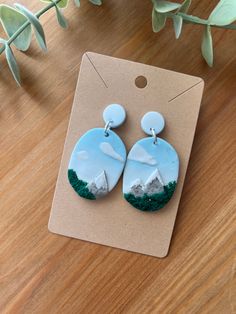 a pair of blue and white earrings sitting on top of a wooden table next to a plant