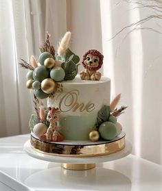 a one tiered cake decorated with animals and greenery on a gold plated stand