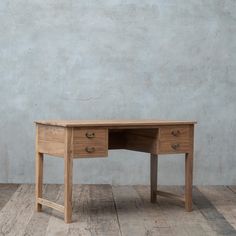 a wooden desk sitting on top of a hard wood floor next to a gray wall