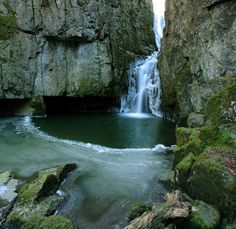 a small waterfall is in the middle of some rocks and mossy water with green algae growing on it