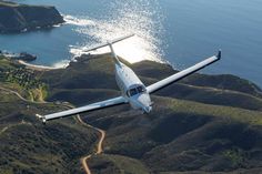 an airplane is flying over the water and land near some hills, with a body of water in the background