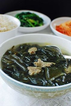 a bowl filled with soup next to bowls of rice and broccoli on a table