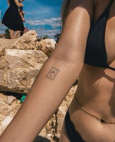 a woman with a tattoo on her arm standing next to some rocks and another person in the background