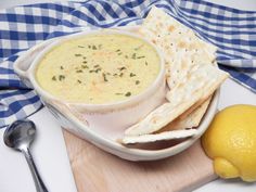 a white bowl filled with soup next to a lemon and crackers on a cutting board