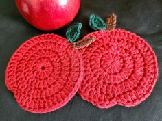 two crocheted apples sitting next to an apple on top of a black surface