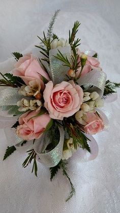 a bouquet of pink roses and greenery on a white tablecloth with silver ribbon