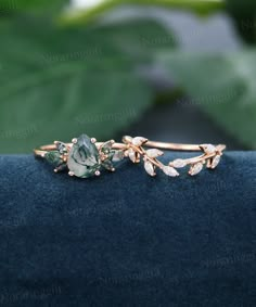 a close up view of a ring with leaves and stones on the side, sitting on top of a blue velvet surface