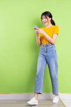 a woman standing in front of a green wall holding a cell phone