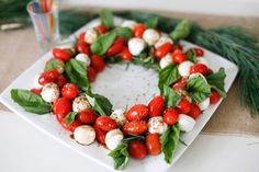 a white plate topped with tomatoes and mozzarella cheese covered in leaves on top of a table