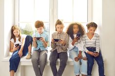 four children are sitting on a window sill looking at their cell phones and texting