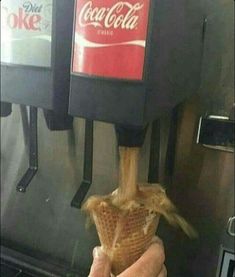 a person is holding an ice cream cone in front of a machine with coca - cola on it