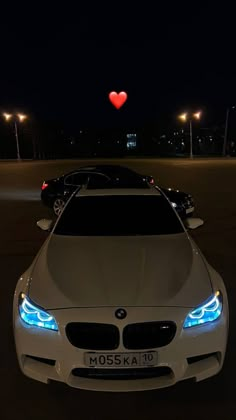 a white car parked in a parking lot at night with a red heart above it