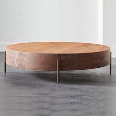 a round wooden table with metal legs on concrete flooring next to white wall and window