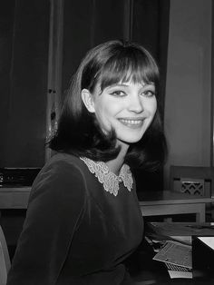 a black and white photo of a woman sitting in front of a computer desk smiling at the camera