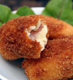 two fried food items on a white plate with green leafy greens in the background