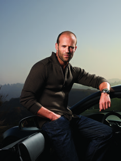 a man sitting on top of a car with his hand on the steering wheel and looking at the camera