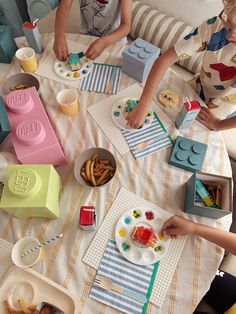 two children sitting at a table with legos and food on the plates in front of them