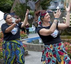 two women are dancing in front of a fountain with their hands up to the sky