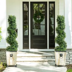 two potted plants sitting on the front steps of a white house with black doors