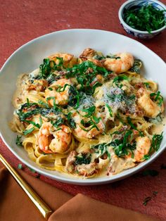 pasta with shrimp, spinach and parsley in a white bowl on a red table