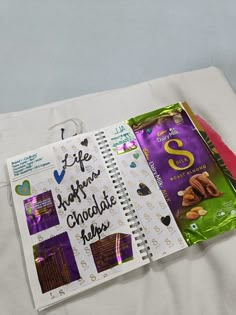 an open notebook with chocolates and candy on the cover is sitting on a bed