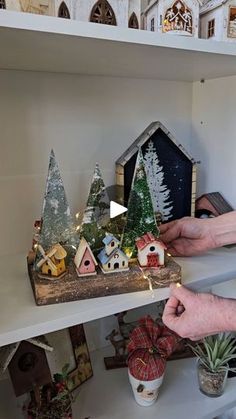 a person is decorating a shelf with christmas trees and small houses on top of it