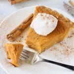 a slice of pumpkin pie with whipped cream on top and cinnamon sticks next to it