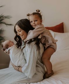 a woman holding a baby on top of her back while sitting on a bed next to a potted plant