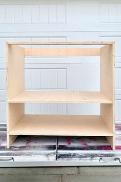 an unfinished shelving unit sitting on top of a piece of plywood paper in front of a garage door