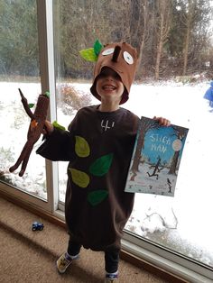 a young boy wearing a costume and holding a book in front of a snowy window