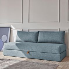 a grey couch sitting on top of a wooden floor next to a white wall and rug