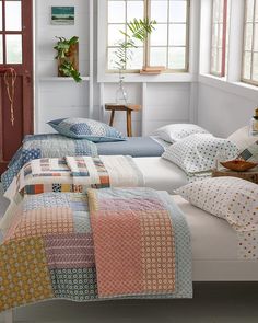 two twin beds with colorful quilts on them in a room next to a window