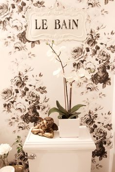 a white toilet sitting in a bathroom next to a wall with flowers and a sign that says le bain