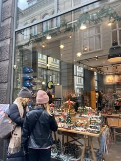 two people standing in front of a store window with christmas decorations on the windowsill