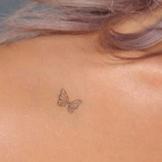 the back of a woman's neck with a small butterfly tattoo on her left shoulder