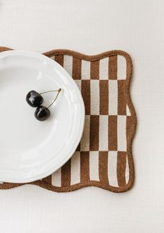 two black cherries on a white plate with brown checkered placemats and utensils