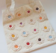 a white tote bag with crocheted flowers on the front and bottom side